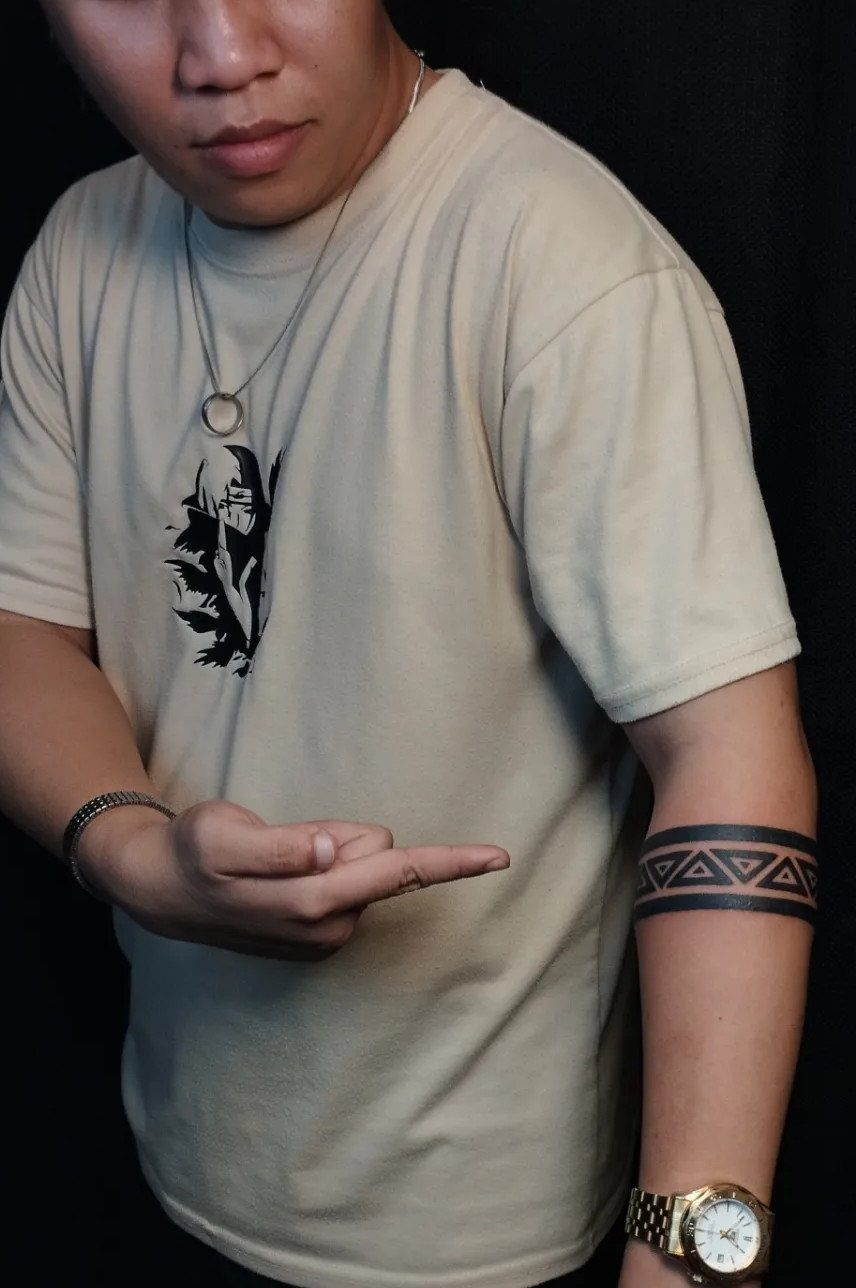 Man pointing to a black geometric arm band tattoo on his left forearm.