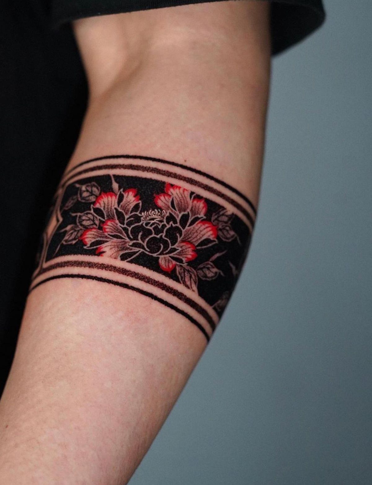 Floral armband tattoo with red flowers and black bands on a person's arm.
