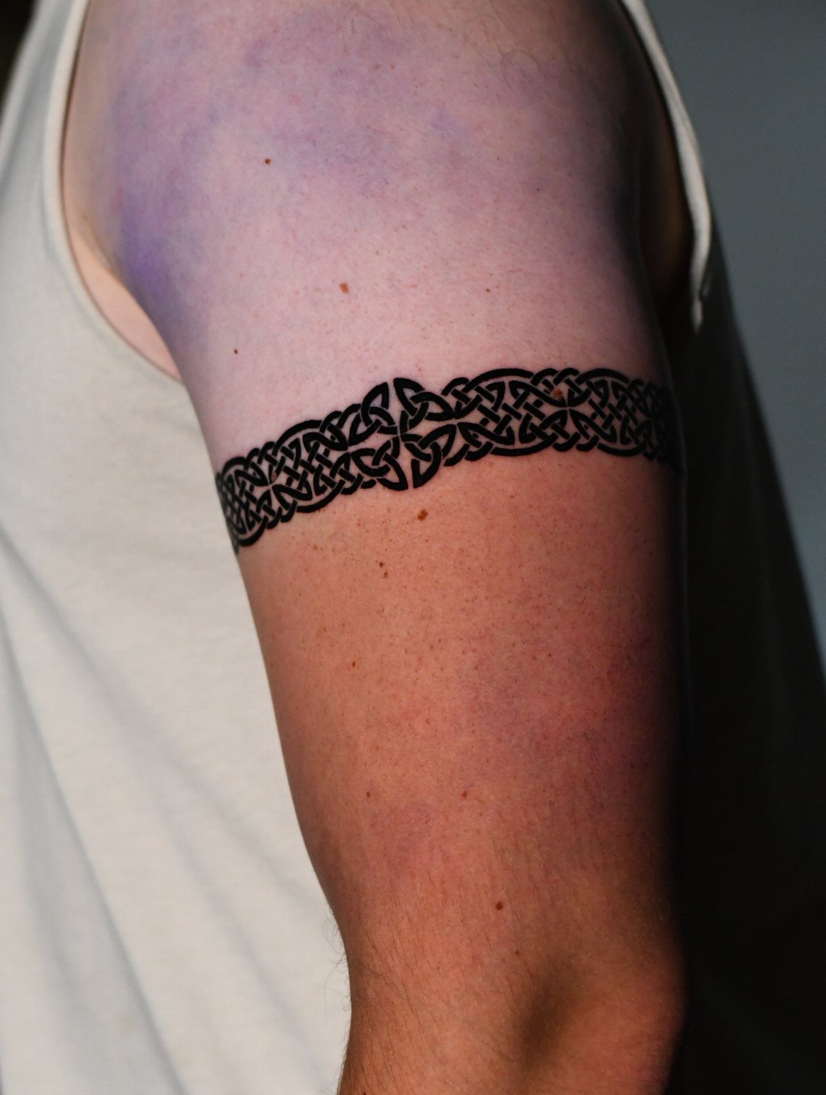 Celtic knot band tattoo wrapping around a person's upper arm bicep