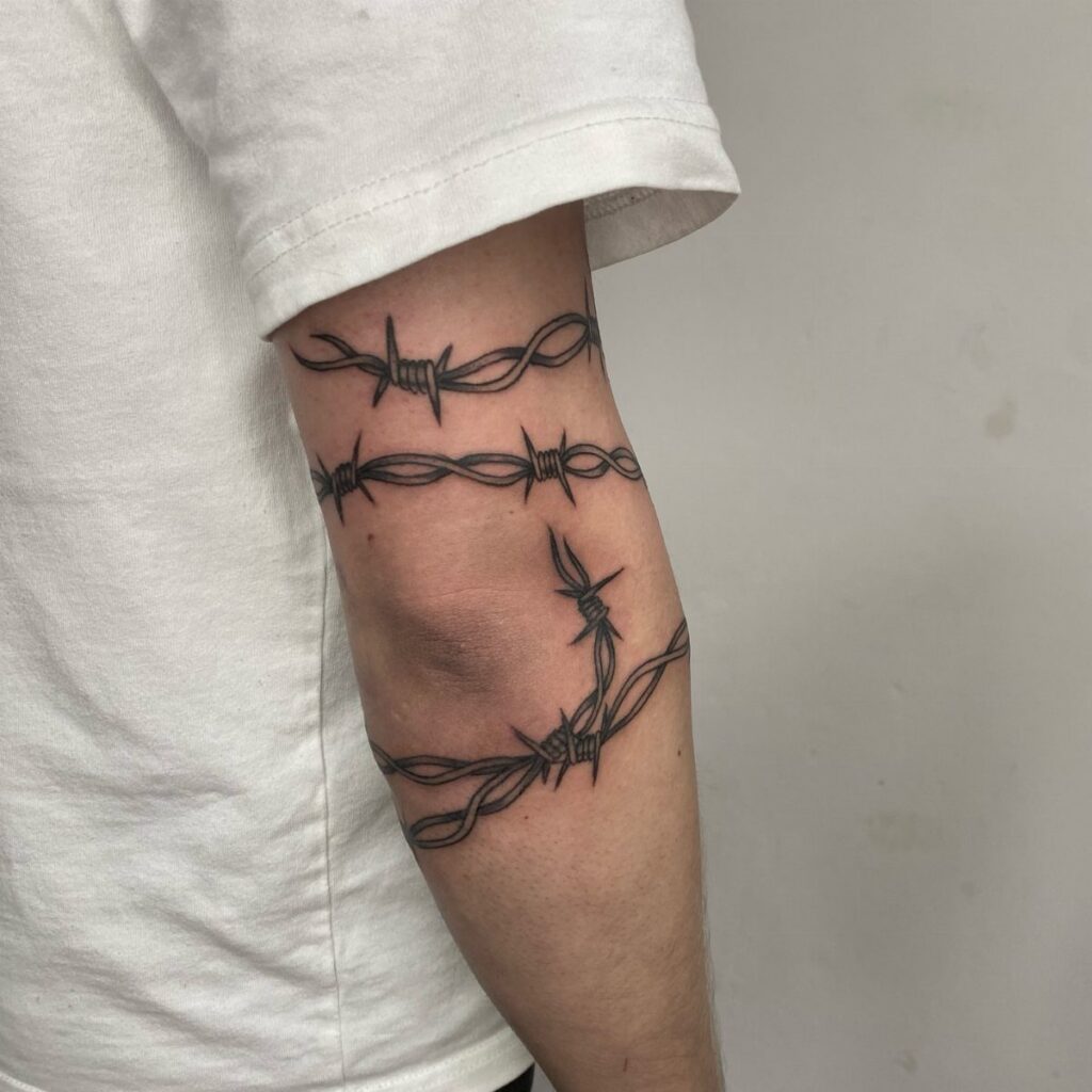Barbed wire tattoos wrapped around a person's upper arm wearing a white shirt.