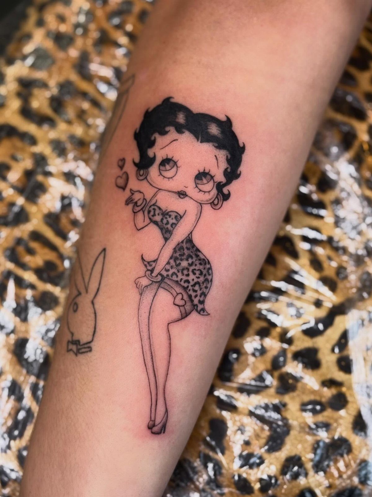 Betty Boop tattoo on a forearm featuring a leopard print outfit and heart.