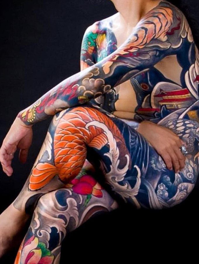 Person with full body suit tattoos featuring colorful koi fish and waves.
