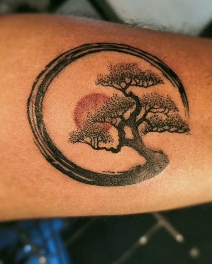 Bonsai tree and red sun tattoo enclosed in a black ink circle.