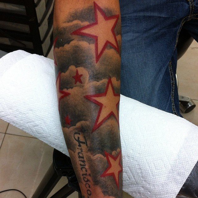 Tattoo of red outlined stars and grey clouds on a person's forearm