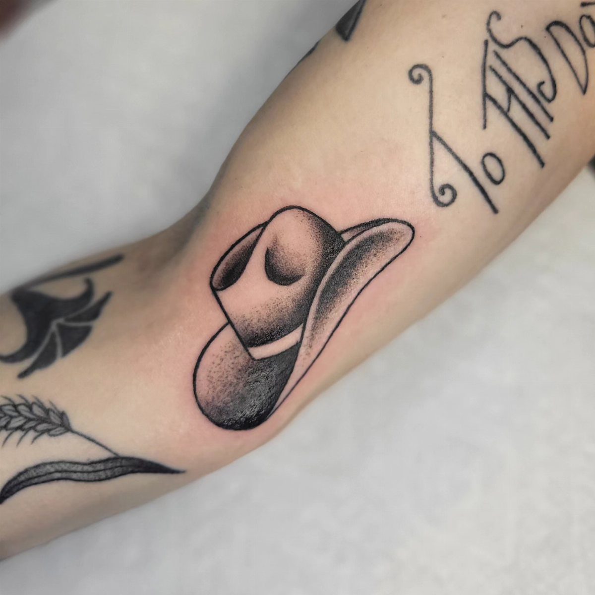 Cowboy hat tattoo with grey shading on a person's forearm skin.