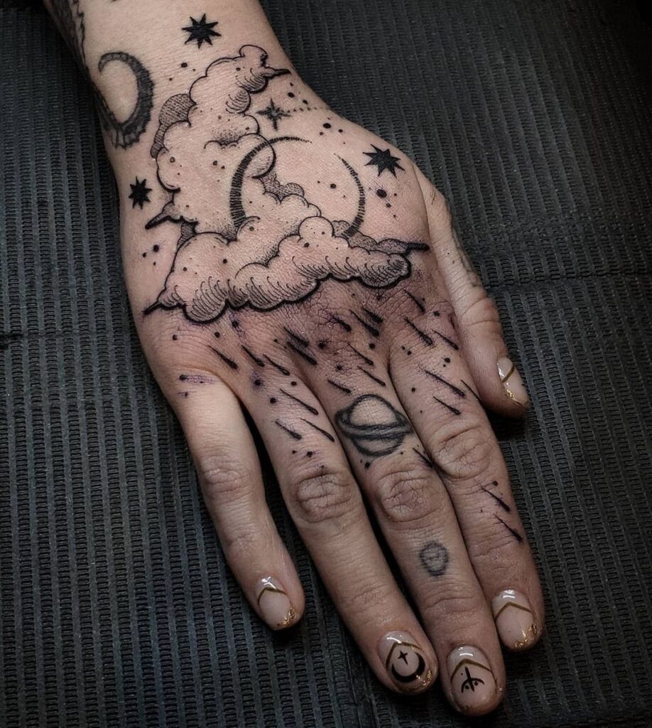 Hand with black ink tattoos of dark clouds, moon, stars, and rain.