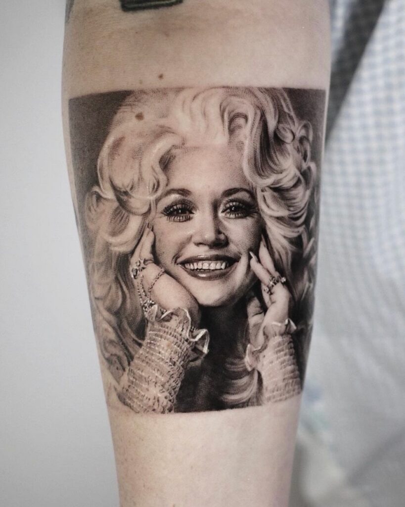 Dolly Parton portrait tattoo in black and grey ink on a person's arm