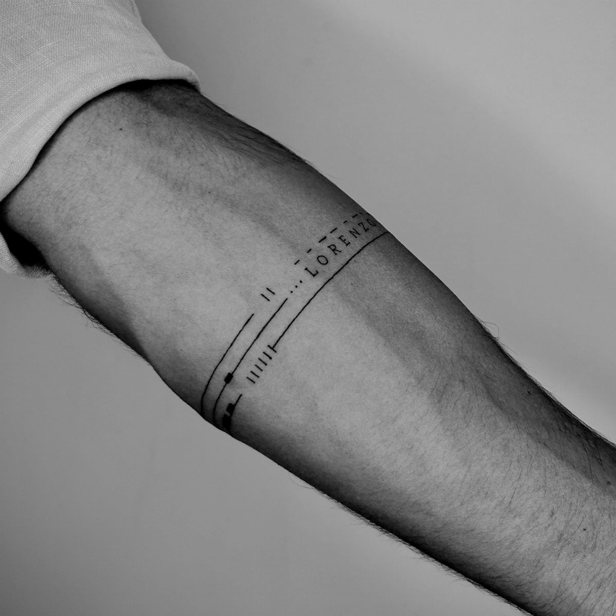 Forearm with a minimalist black band tattoo featuring the name Lorenzo and geometric lines.