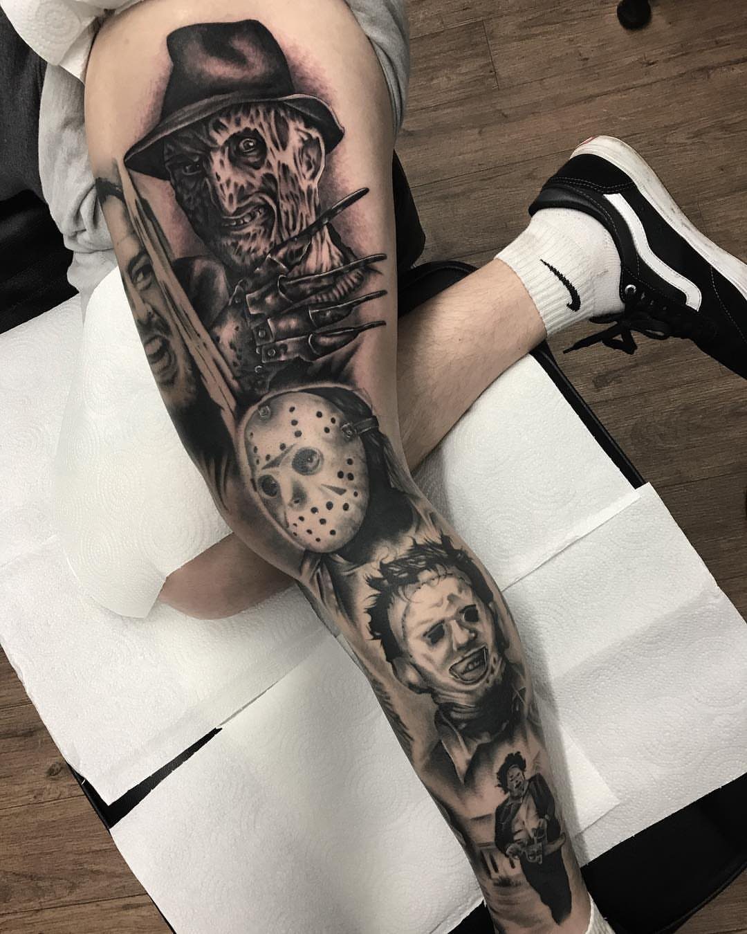 Freddy Krueger and other horror movie characters tattooed in black and grey on a leg