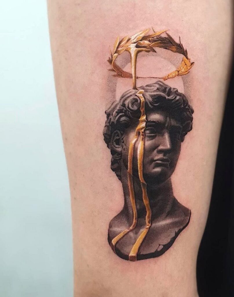 Tattoo of a stone bust with gold ink laurel wreath and gold streaks.