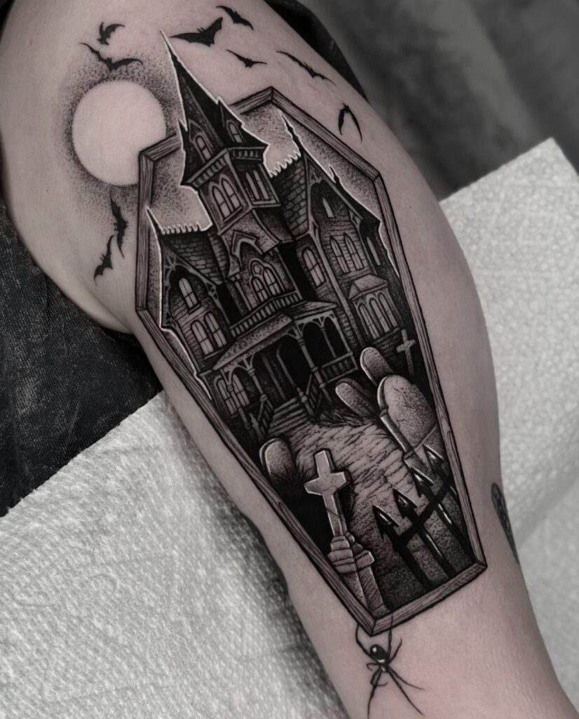 Haunted house tattoo in a coffin frame with bats and a graveyard.
