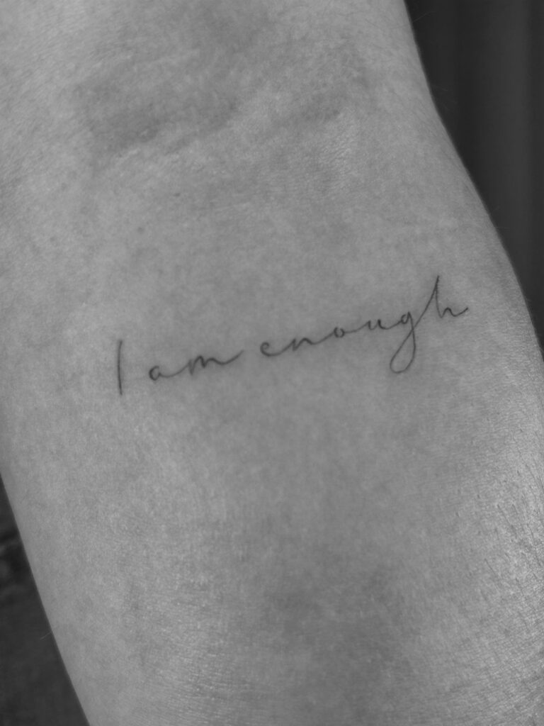 Cursive tattoo reading I am enough on a person's skin in black and white.