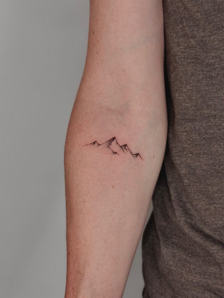 Minimalist mountain range tattoo with thin black lines on a person's forearm.