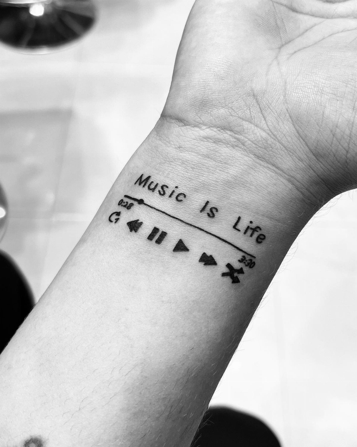 Wrist tattoo with the words Music Is Life and a music player interface.