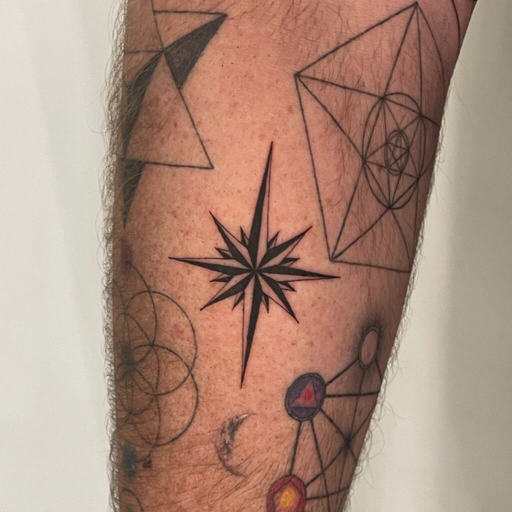 North star tattoo centered among geometric black ink designs on a person's arm.