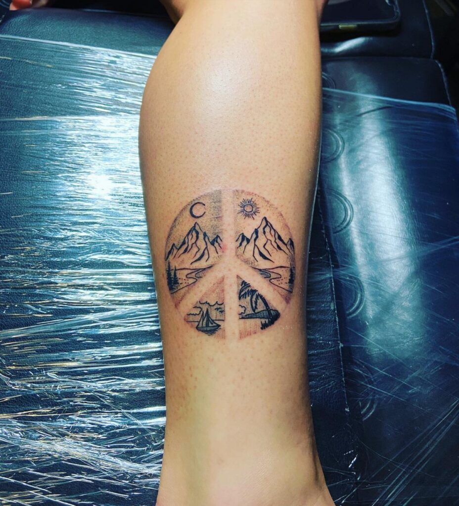 Peace sign tattoo on a leg featuring mountain landscapes, sun, and moon.