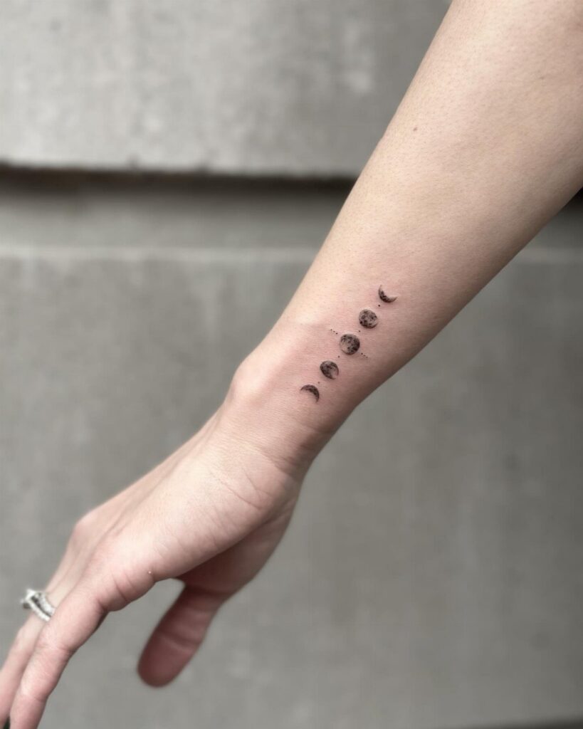 Moon phases tattoo in black ink on a person's inner wrist.