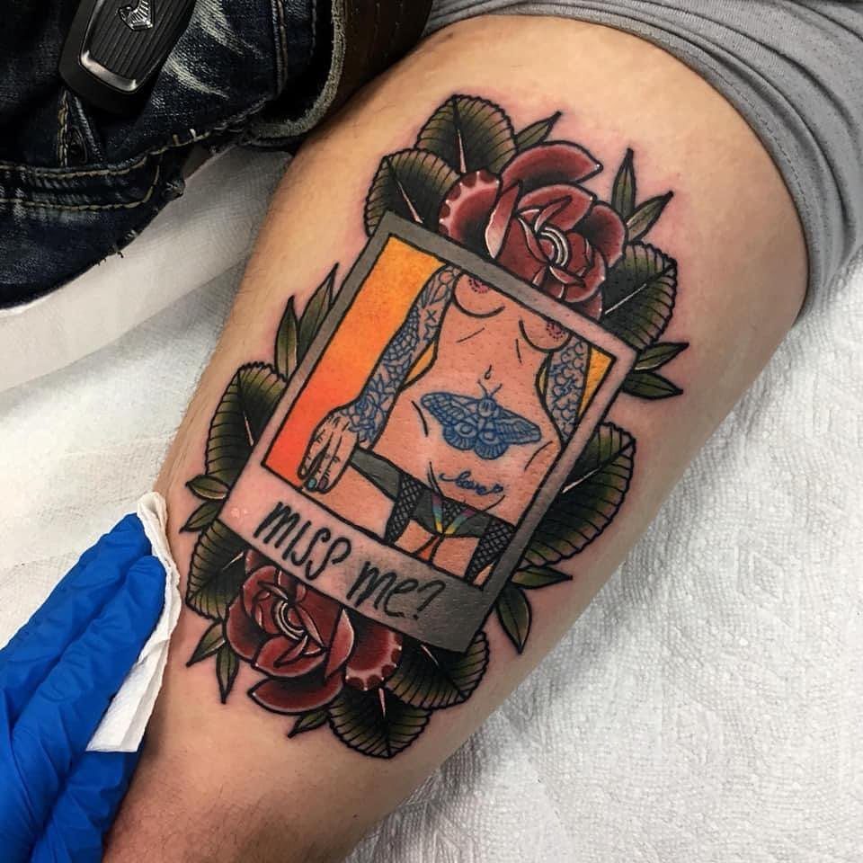 Pin up girl tattoo inside a polaroid frame with red roses on a thigh