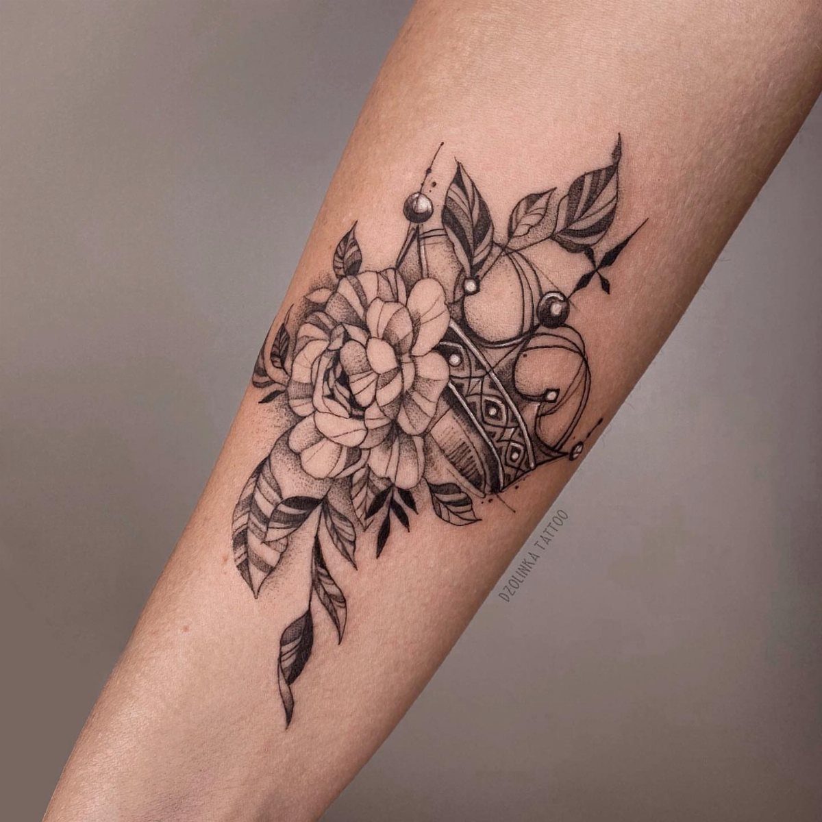 Queen crown tattoo with a flower and leaves on a person's forearm.