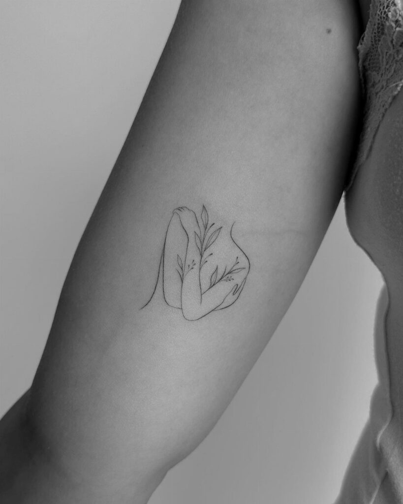 Fine-line tattoo of a female body silhouette with leaves on an upper arm.