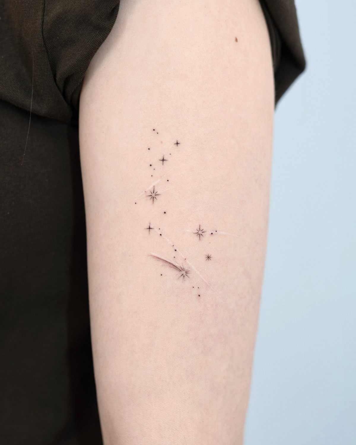 Minimalist shooting star tattoo with small black stars on a person's upper arm.