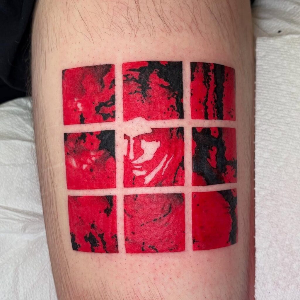 Red and black grid tattoo on skin featuring a stylized face in center