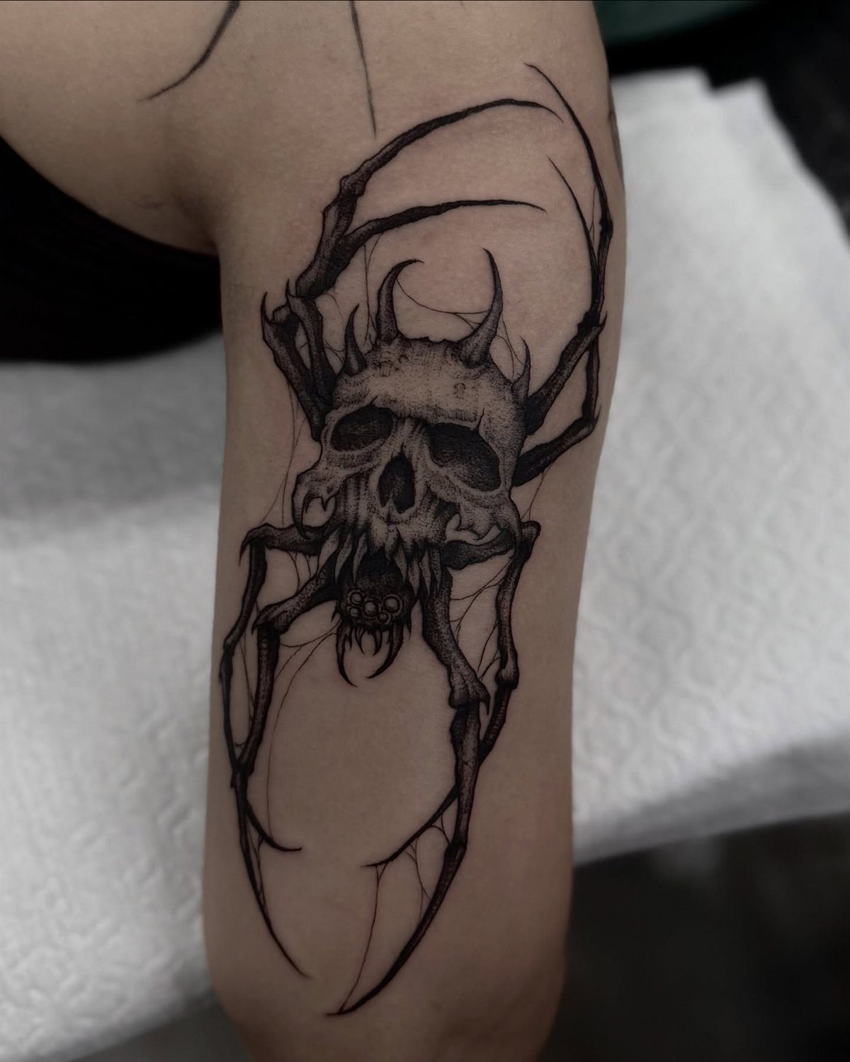 Spider skull tattoo on a forearm with long spindly legs and dark shading.