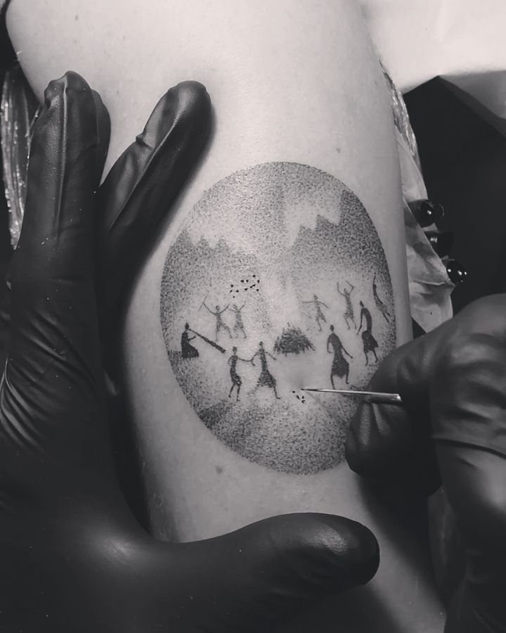 Stick poke tattoo process showing a needle creating a dot-work prehistoric scene on skin.