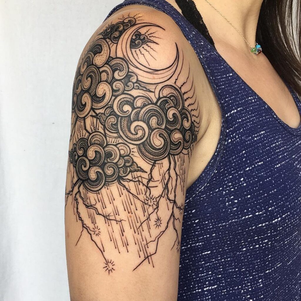 Storm cloud tattoo with a crescent moon and lightning on an upper arm.