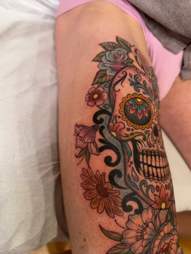 Colorful sugar skull tattoo with roses and flowers on a person's leg