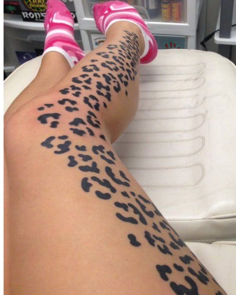 Cheetah print tattoo covering a person's leg from thigh to ankle on white table.