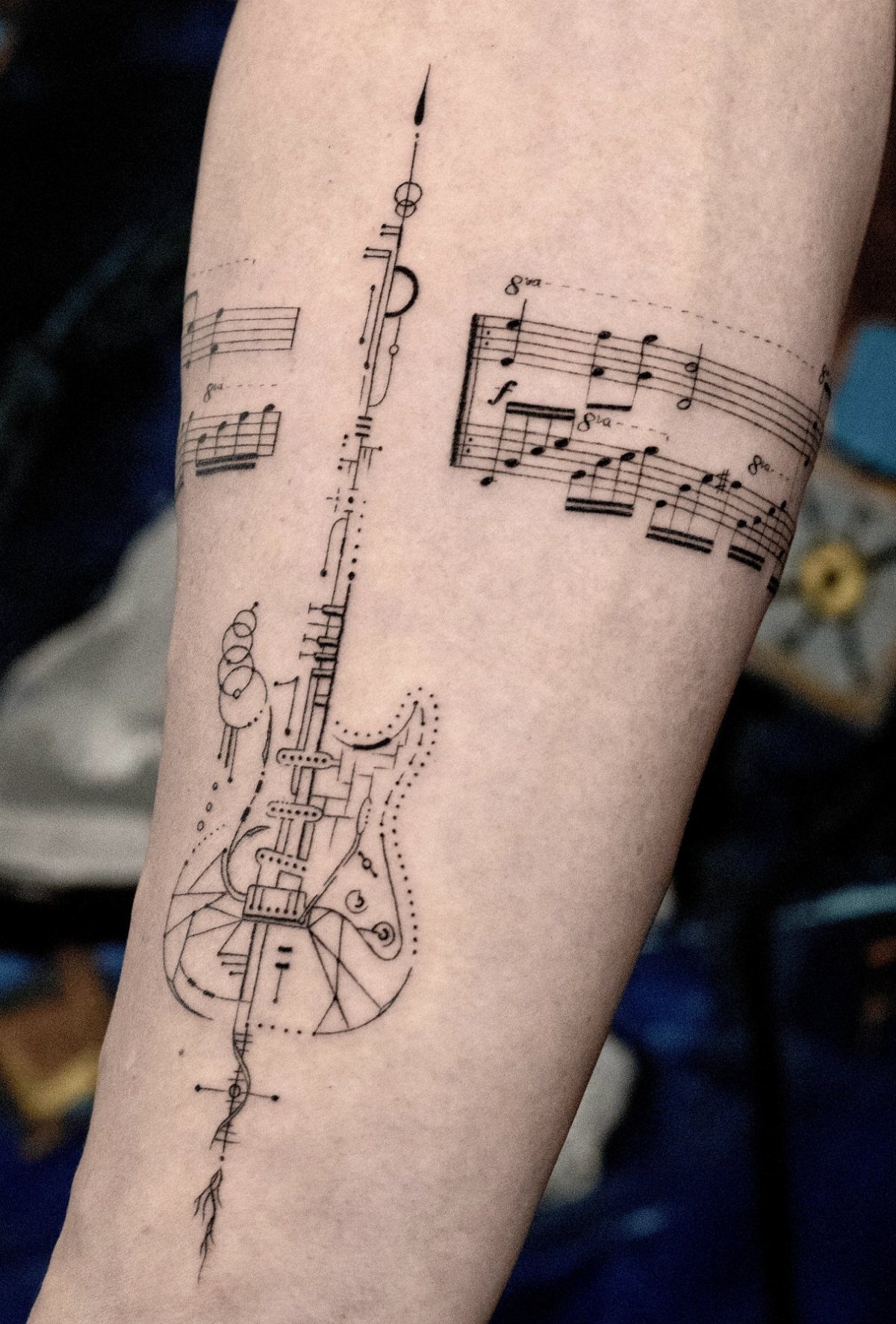 Electric guitar tattoo with musical notes and geometric lines on a person's forearm