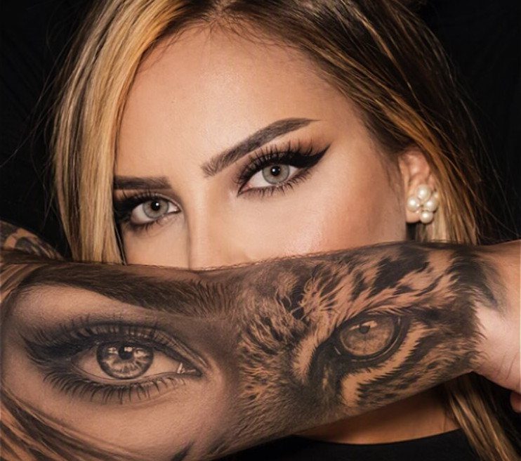 Woman's arm featuring a realistic tattoo of a human eye and an owl eye.