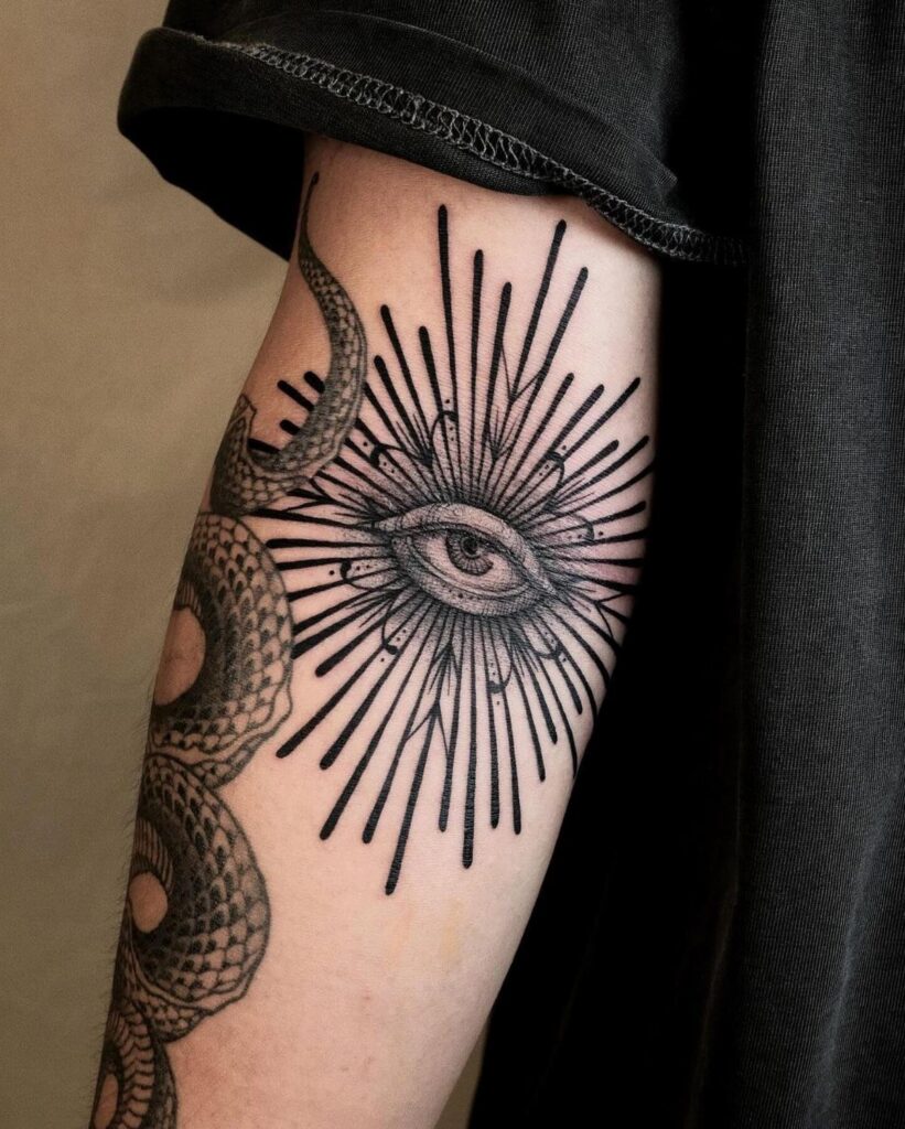 Eye tattoo with radiating lines and a snake on a person's forearm