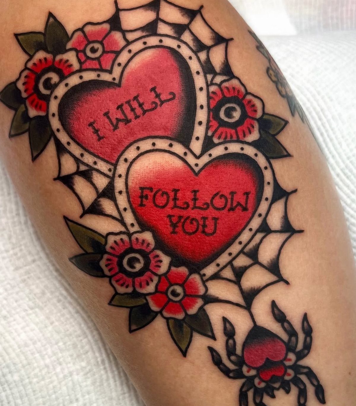Traditional red heart tattoos with text and a spider web on skin.