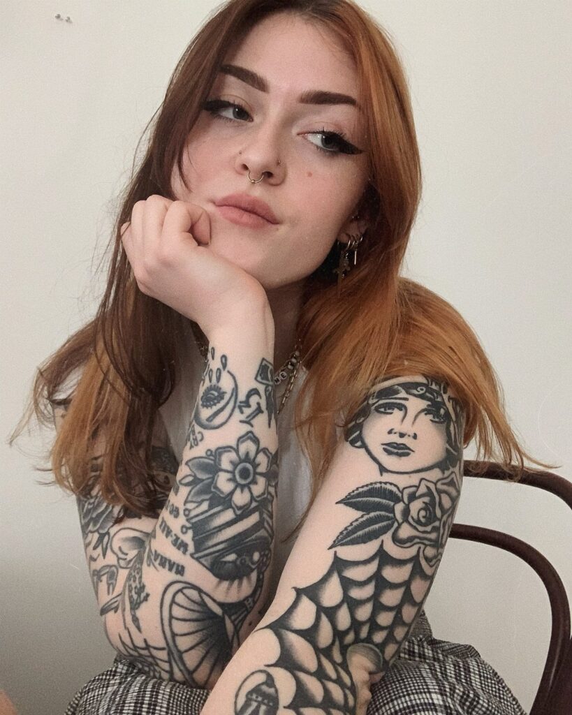 Woman with reddish-brown hair showing bold traditional black ink tattoos on her arms.