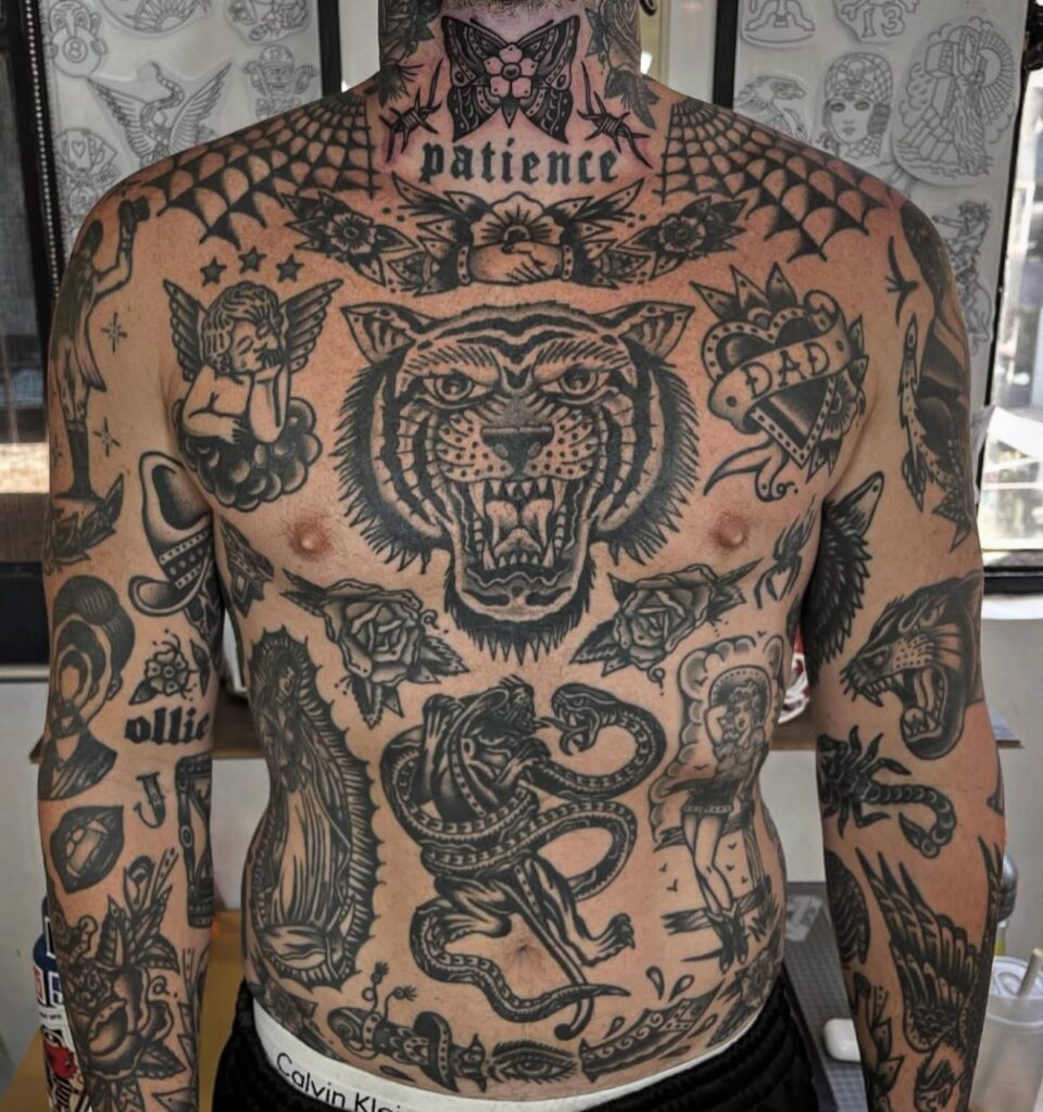 Man's torso and arms covered in black ink traditional tattoos including a tiger head.