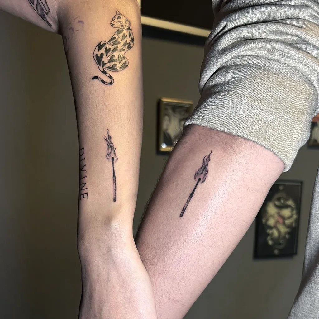 Two forearms with matching small black flame tattoos side by side.