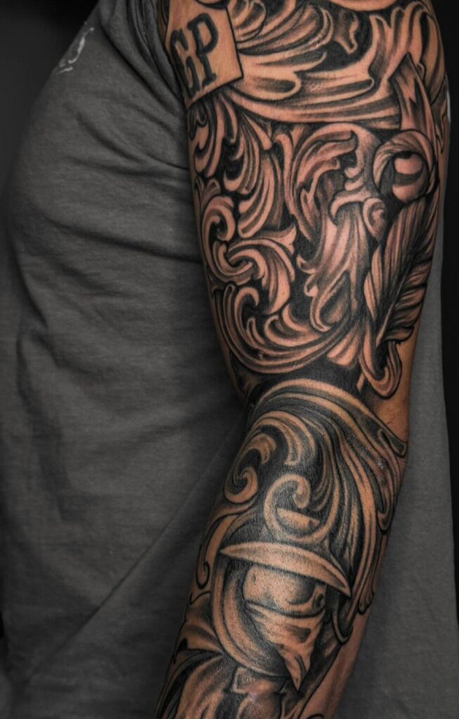 Tattoo on an arm with intricate black and grey western leather tooling patterns.