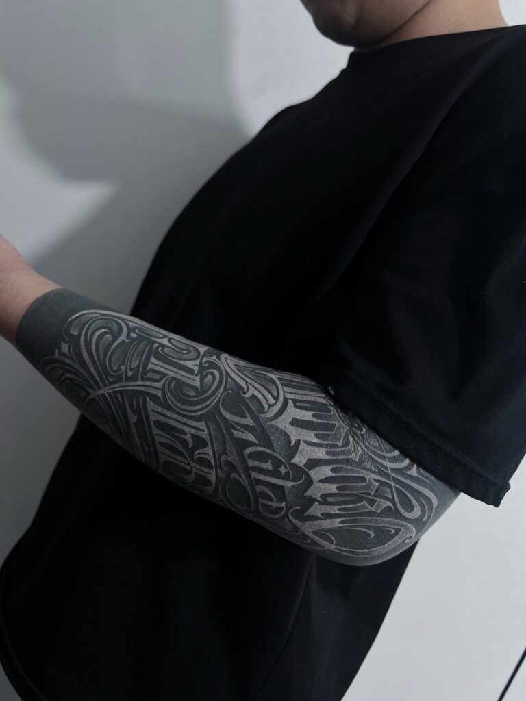 Forearm tattoo with white ink designs and lettering over a solid black background.