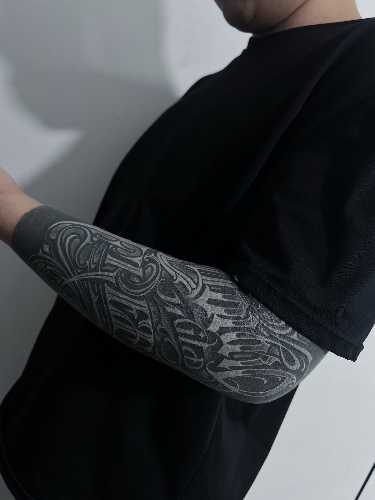 Forearm tattoo with white ink designs and lettering over a solid black background.